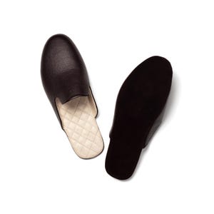 May include: A pair of brown leather slippers with a quilted white lining. The slippers are shown from above, with one slipper turned to show the sole.