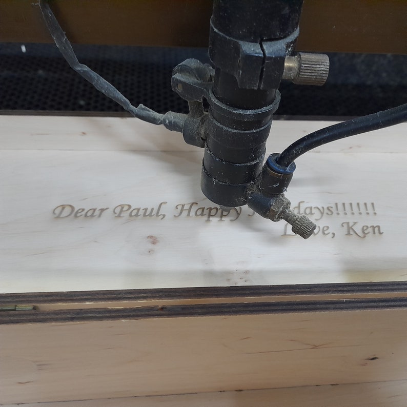 May include: A laser engraver is engraving a wooden box with the message "Dear Paul, Happy days!!!!! Love, Ken".