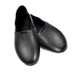 May include: A pair of black leather ballet slippers. The shoes are smooth and have a rounded toe. The slippers are designed to be worn by dancers. The shoes are shown on a white background.