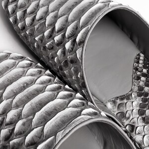 May include: A pair of gray snakeskin slippers with a pointed toe and a closed back. The slippers are made of soft, supple leather and have a comfortable fit.