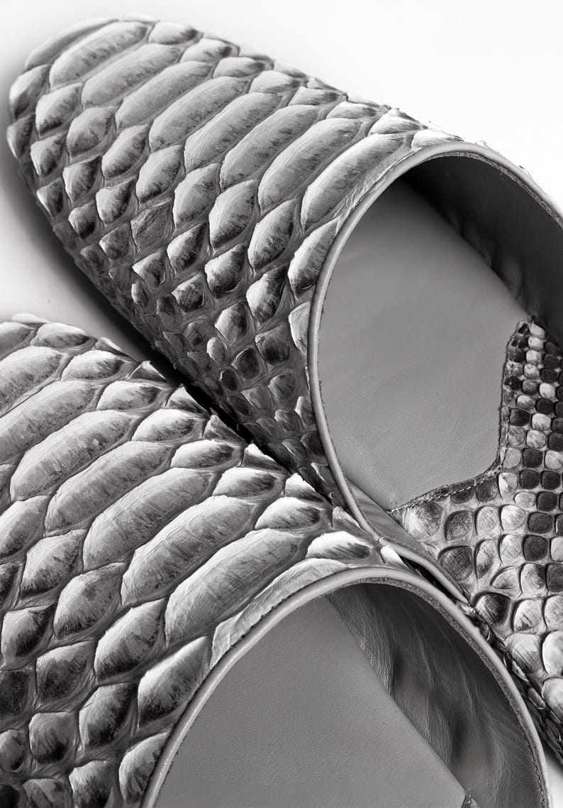 May include: A pair of gray snakeskin slippers with a pointed toe and a closed back. The slippers are made of soft, supple leather and have a comfortable fit.