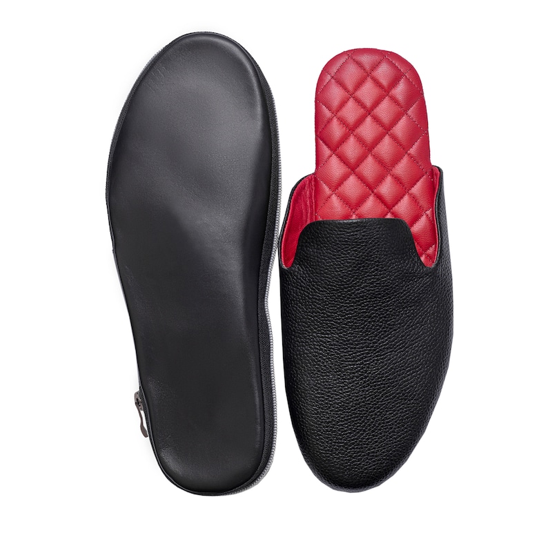 May include: Black leather slipper with a red quilted interior, next to a matching black zippered case. The slipper has a textured exterior and a rounded toe. The case is designed to hold the slipper for travel or storage.