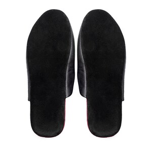 May include: A pair of black leather slippers, viewed from the bottom, showcasing a textured surface. The interior features a soft, dark material with a red accent along the edges. The design is simple and elegant.