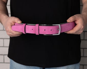 May include: A pink suede belt with a silver buckle. The belt is held in the hands of a person.