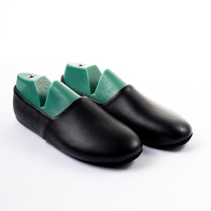 May include: A pair of black leather loafers with green shoe trees inside. The shoes are displayed on a white background. The loafers have a rounded toe and a low profile.