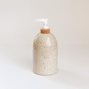 Wheel-thrown, speckled stoneware soap pump with cork sleeve and white plastic pump on white background