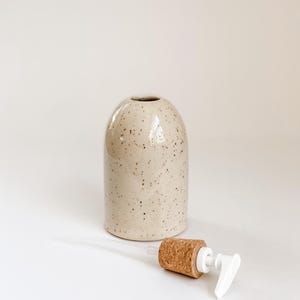 Wheel-thrown, speckled stoneware soap pump with cork sleeve  and white plastic pump removed from container, sitting in foreground on white background