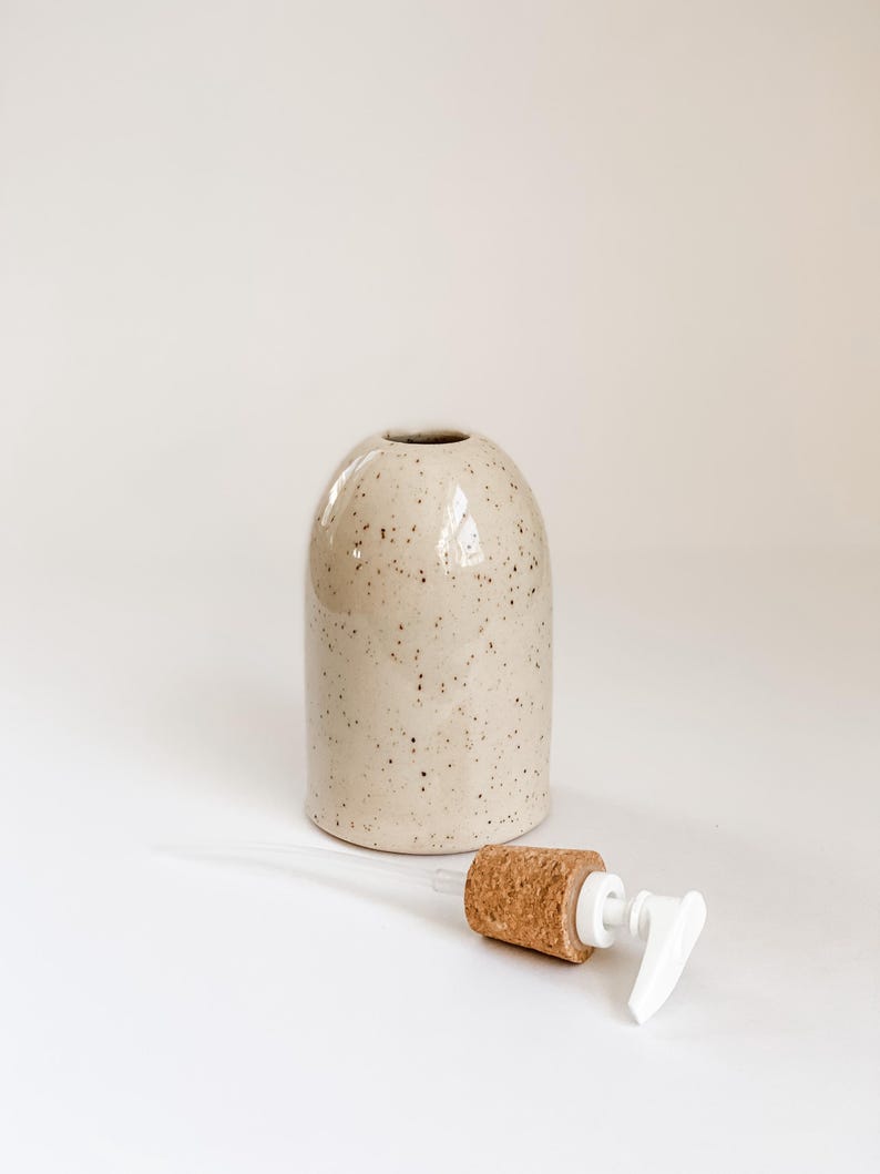 Wheel-thrown, speckled stoneware soap pump with cork sleeve  and white plastic pump removed from container, sitting in foreground on white background