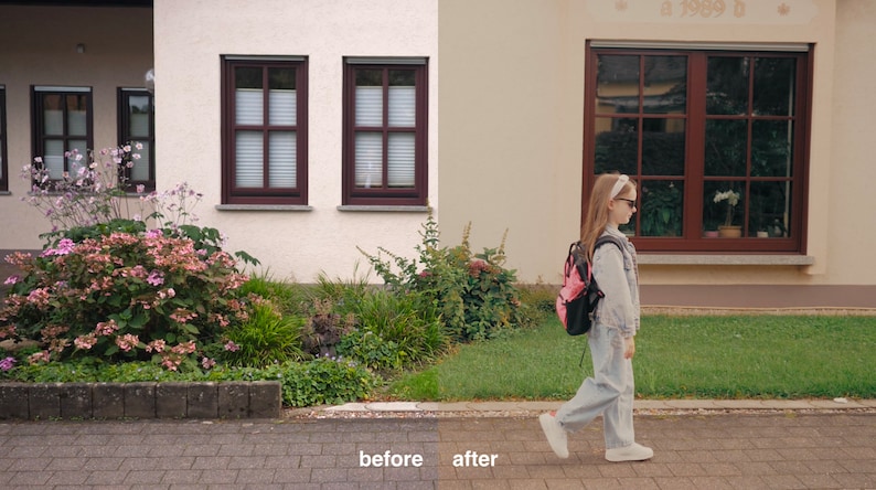 May include: A young person wearing a denim jacket and jeans walks down a sidewalk in front of a house with a pink backpack. The house has two windows with brown frames and a large window with a brown frame on the right side of the image.