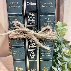 May include: Four dark green hardcover books with gold lettering and illustrations. The books are stacked vertically and tied together with twine. The titles of the books are "Riptide", "Collision", "Wild Goose, Brother Goose", "The Copper Beech", "Equation", "I Can Jump Puddles", "The Hills Are Lonely", and "Go In and Sink!" The books are all Reader's Digest Condensed Books.