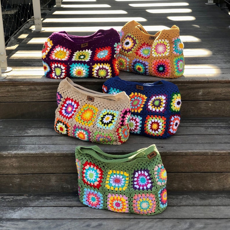 May include: Five colorful crochet tote bags with square patterns in various colors, including purple, tan, blue, gold, and green. Each bag features a unique combination of bright, cheerful colors and a small label.
