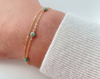 May include: A gold chain bracelet with small green gemstone beads.