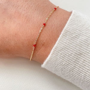 May include: A delicate gold chain bracelet with small red beads. The bracelet is on a person's wrist.