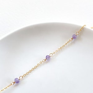 May include: A delicate gold chain necklace with three small purple gemstone beads.