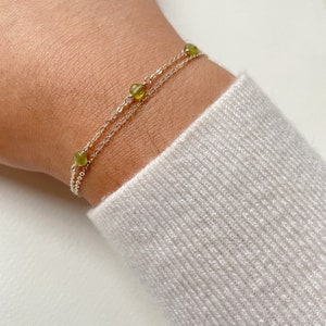 May include: A delicate silver chain bracelet with small green gemstone beads. The bracelet is layered with two chains, creating a stylish and minimalist look.