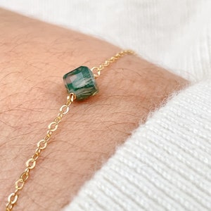 May include: A delicate gold chain bracelet featuring a single green agate gemstone pendant. The agate has a unique swirling pattern.