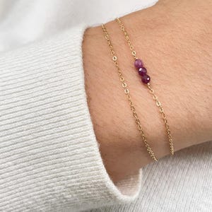 Peut inclure: Un bracelet délicat en chaîne dorée avec trois petites perles de pierres précieuses rose foncé.