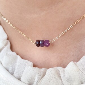 May include: A gold chain necklace with three purple gemstone beads.