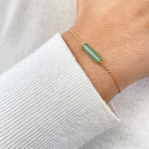 May include: A gold chain bracelet with a single green stone bar charm.