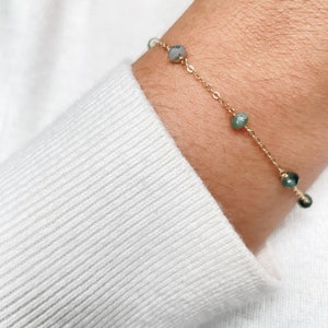 May include: A delicate gold chain bracelet with small, round, green and grey gemstone beads.