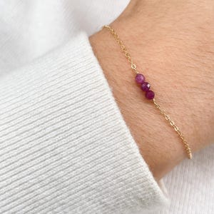 Peut inclure: Un bracelet délicat en chaîne dorée avec trois petites pierres rondes roses.