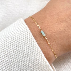 May include: A delicate gold chain bracelet with three small light blue gemstone beads.