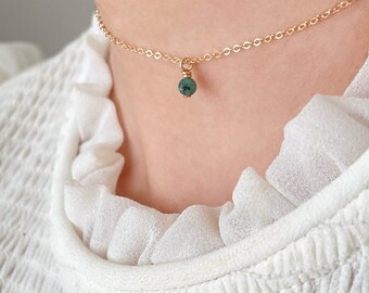 May include: A delicate gold chain necklace with a small, round green gemstone pendant.