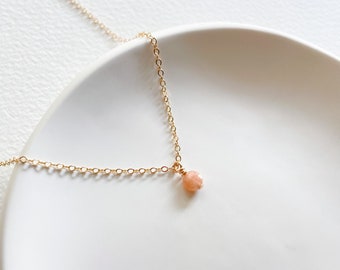 May include: A delicate gold chain necklace with a small, round, peach-coloured gemstone pendant.