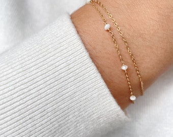 May include: A gold chain bracelet with small white beads. The bracelet is layered with two chains.