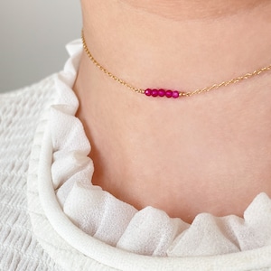 May include: A delicate gold chain necklace with a row of small, bright pink beads.