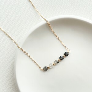May include: A gold chain necklace with a row of five round, clear and black gemstone beads.