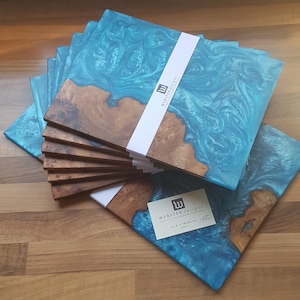 May include: A stack of rectangular serving boards made from natural wood burl and swirling turquoise blue resin. Each board features a white paper band with the text WEBSTER DESIGNS. A small white business card with the same logo is included.