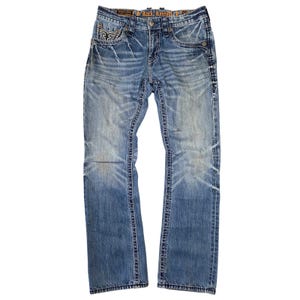 May include: Light blue denim jeans with a faded wash and distressed details. Features decorative stitching, front and back pockets, and the brand name "Rock & Republic" on the waistband. The jeans have a classic five-pocket design.