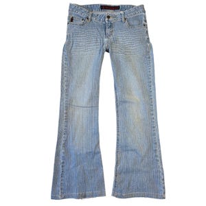 May include: Light blue denim jeans with a low rise and flared leg. The jeans have a classic five-pocket design, a button and zipper closure, and belt loops. The denim has a subtle vertical texture.