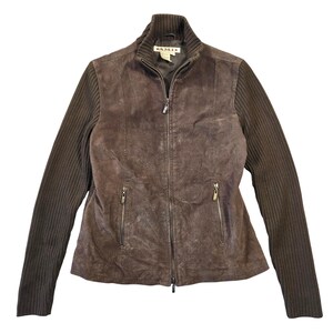 May include: A dark brown zip-up jacket featuring a suede leather front panel and ribbed knit sleeves. The garment includes a high collar, a full-length front zipper, and two zippered side pockets. A label with the text A.M.I. is visible at the neck.