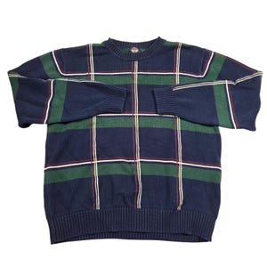 May include: A navy blue sweater with a green and white plaid pattern. The sweater has long sleeves and a ribbed hem and cuffs. The plaid design includes thin red lines. The sweater is made of a soft, knitted material.