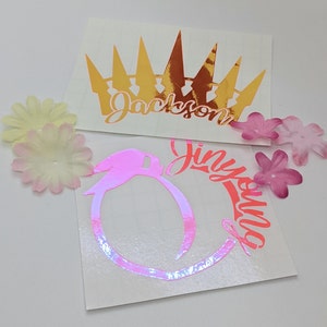 May include: Two vinyl stickers with names and designs. The first sticker is gold and features a crown with the name "Jackson" underneath. The second sticker is pink and features a peach with the name "Jinyuila" around it.