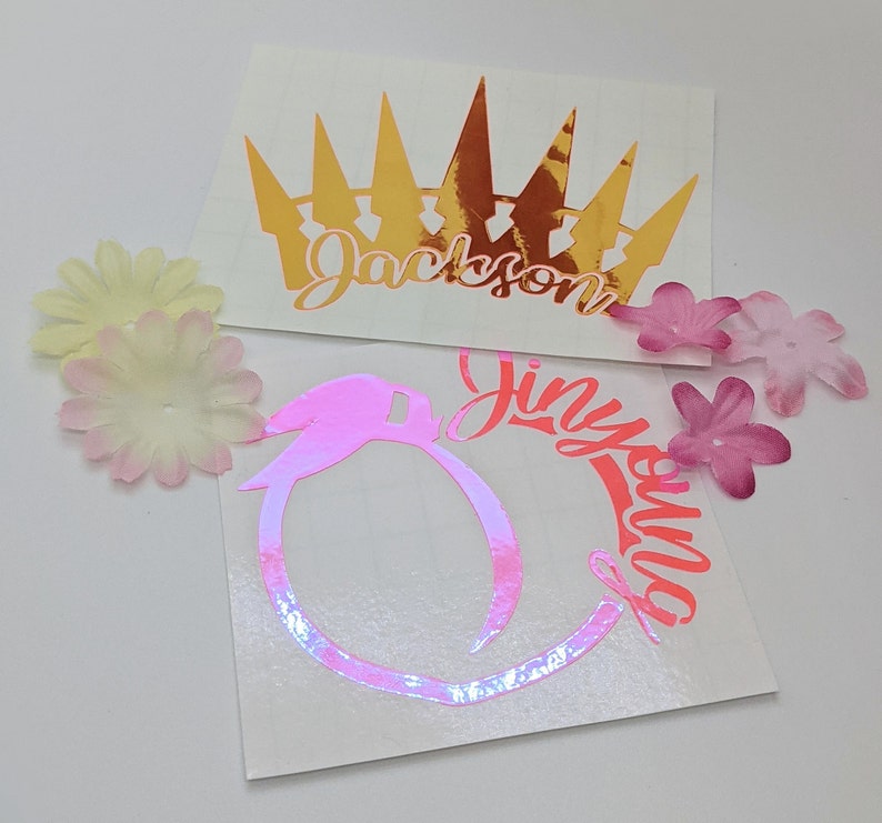 May include: Two vinyl stickers with names and designs. The first sticker is gold and features a crown with the name "Jackson" underneath. The second sticker is pink and features a peach with the name "Jinyuila" around it.