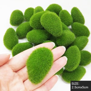 Op de afbeelding: Een stapel van 25 groene mosstenen, elk met een afmeting van 2,5 cm bij 5 cm. De stenen zijn gemaakt van zacht, groen mosmateriaal en zijn perfect om een vleugje natuur aan uw interieur toe te voegen.