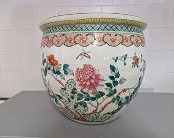 May include: A large, white ceramic planter with a floral design. The planter has a wide, round base and a narrow opening. The floral design features pink, red, and green flowers and leaves.