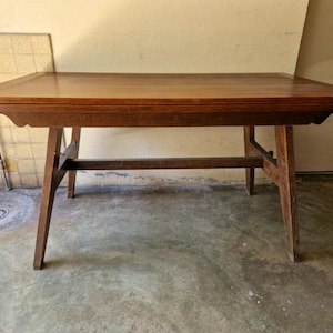Peut inclure: Table rectangulaire en bois brun foncé. Elle possède quatre pieds inclinés et une barre de support inférieure. Le plateau a un bord légèrement surélevé. La table mesure environ 150 cm de long.