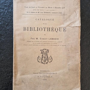 Puede incluir: Una portada de catálogo antiguo en francés, que muestra signos de edad y desgaste. La portada es de color marrón claro descolorido. El título "CATALOGUE DE LA BIBLIOTHÈQUE" es visible. El texto incluye la fecha "1918" y el nombre "M. Ernest Labadie".