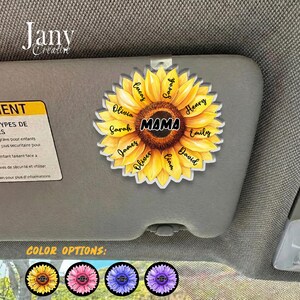 May include: A sunflower-shaped car visor clip with the word "MAMA" in the center, surrounded by names. The clip is yellow with a brown center and includes the names Lucas, Olivia, Sarah, James, Oliver, Liam, David, Emily, Henry, and Sarah.