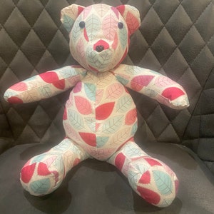 May include: A handmade teddy bear with a pink, white and blue leaf pattern. The bear has black button eyes and a black nose.