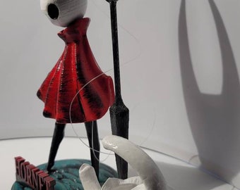 May include: A 3D-printed figurine of a character with a white head, red dress, and black legs, holding a black sword. The base is teal with the word "HORNET" in red. A second white head lies on the surface.