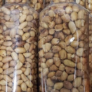 May include: A close-up of several glass jars filled with roasted peanuts. The jars are clear and show the peanuts inside. The peanuts are a light brown color and appear to be salted.