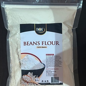 May include: A white plastic bag filled with white bean flour. The bag has a black label with the text "BOJ Foods" and "Beans Flour 100% Beans". The label also includes instructions on how to prepare the flour and a small image of white beans in a bowl.
