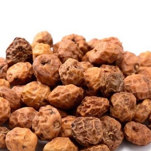 May include: A pile of dried tiger nuts, also known as chufa nuts, against a white background. The nuts are a mix of light and dark brown, with a wrinkled, textured surface. They are a popular snack and ingredient in various cuisines.