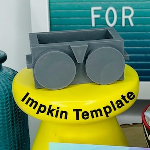 May include: Gray plastic doll glasses template on a yellow stand with the text "Impkin Template". A business card with the text "Stitches & Whimsy Handmade" is on a wooden surface with a pair of blue and silver pliers.