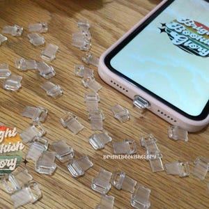 May include: A close-up of a table with a large number of clear plastic book page holders. The holders are scattered across the table. A pink phone case with the text "Bright Bookish Glory" is visible in the background.